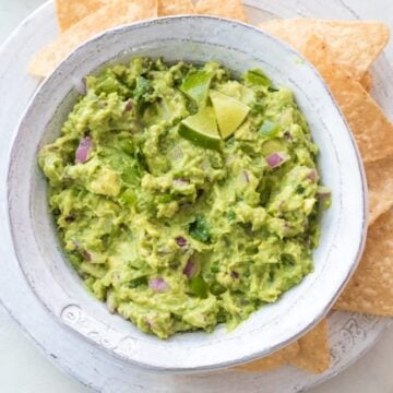 Homemade Chipotle guacamole served in a white bowl with tortilla chips on a white plate.