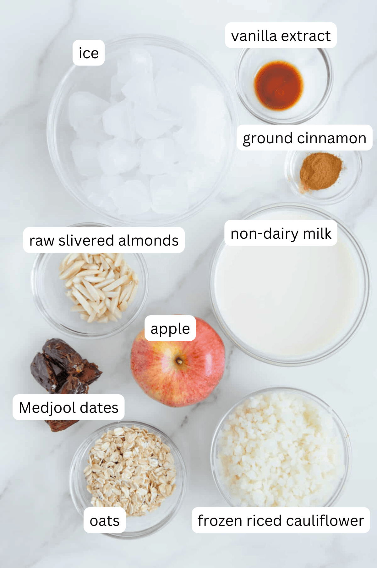 Ingredients of a vegan apple pie smoothie with a white marble background.