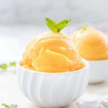Homemade mango sorbet garnished with fresh mint in a white dish with a gray background.