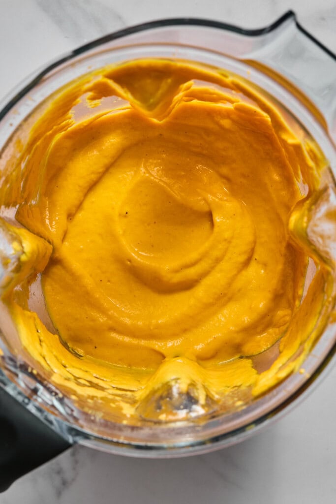 Bright orange creamy sauce or dip in a blender, viewed from above, with smooth texture and some streaks along the glass sides—perfect as a base for Creamy Vegan Pumpkin Garlic Pasta.