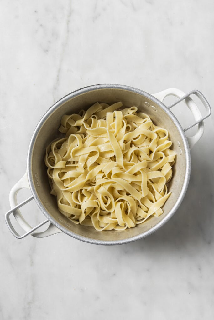 A white pot filled with creamy Vegan Garlic Mushroom Fettuccini sits on a light marble surface.