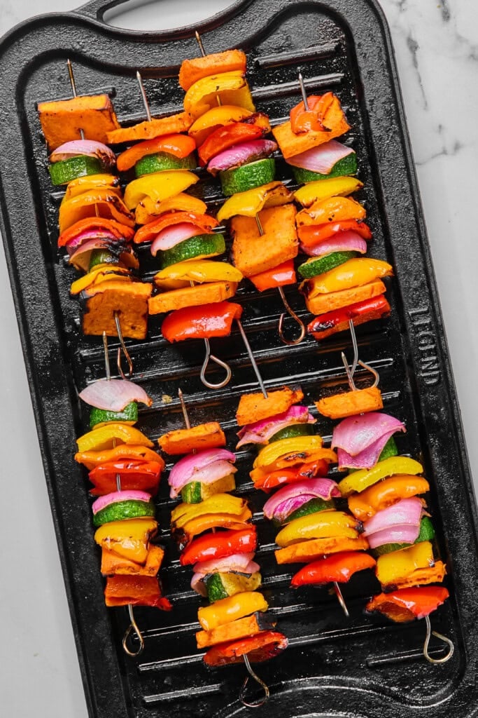 Rainbow Veggie Kebabs: Colorful vegetable skewers, including zucchini, red onion, red and yellow bell peppers, and sweet potato chunks, arranged neatly on a black grill pan.