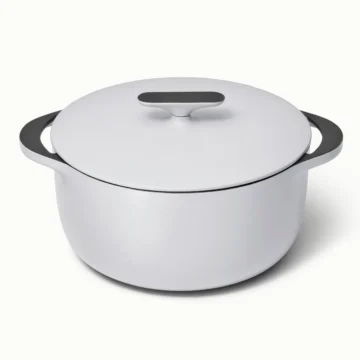 A white lidded Dutch oven crafted from non-toxic enameled cast iron, featuring large black handles on both sides, sits elegantly on a plain light background.