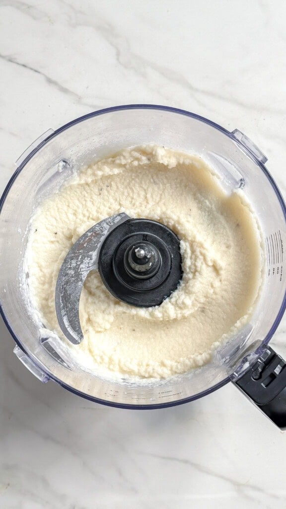 A food processor bowl containing a smooth, creamy white vegan mashed cauliflower.