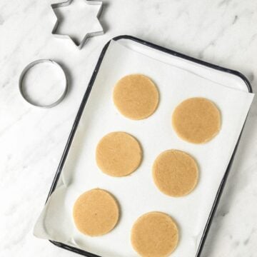 Vegan gluten-free sugar cookies on a baking sheet lined with parchment paper with a white marble background.