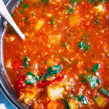 Vegan minestrone soup with quinoa in a black bowl with a blue background.