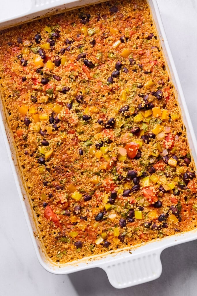A white baking dish filled with a colorful Vegan Mexican Casserole featuring quinoa, black beans, diced tomatoes, bell peppers, and a golden, slightly crispy top.