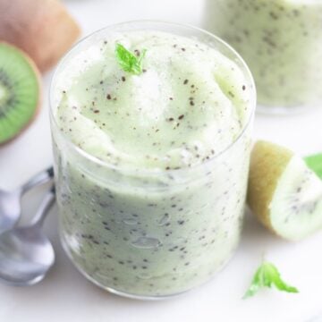 Kiwi smoothie garnished with fresh mint on a white serving platter next to fresh kiwi.