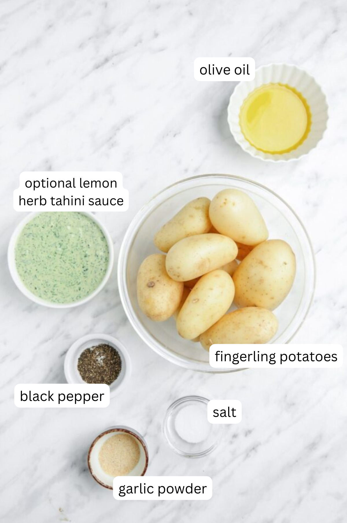 Ingredients for extra crispy smashed fingerling potatoes on a white marble background.