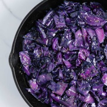 Sautéed purple cabbage in a cast iron pan with a marble white background.