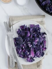 Sautéed purple cabbage on a white plate with a fork and knife.