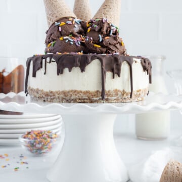 Vegan ice cream cake on a white cake platter topped with a magic chocolate shell and scoops of vegan chocolate ice cream with upside down ice cream cones overtop.