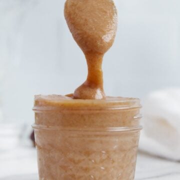 A spoonful of vegan caramel sauce dripping into a glass container of vegan caramel sauce.