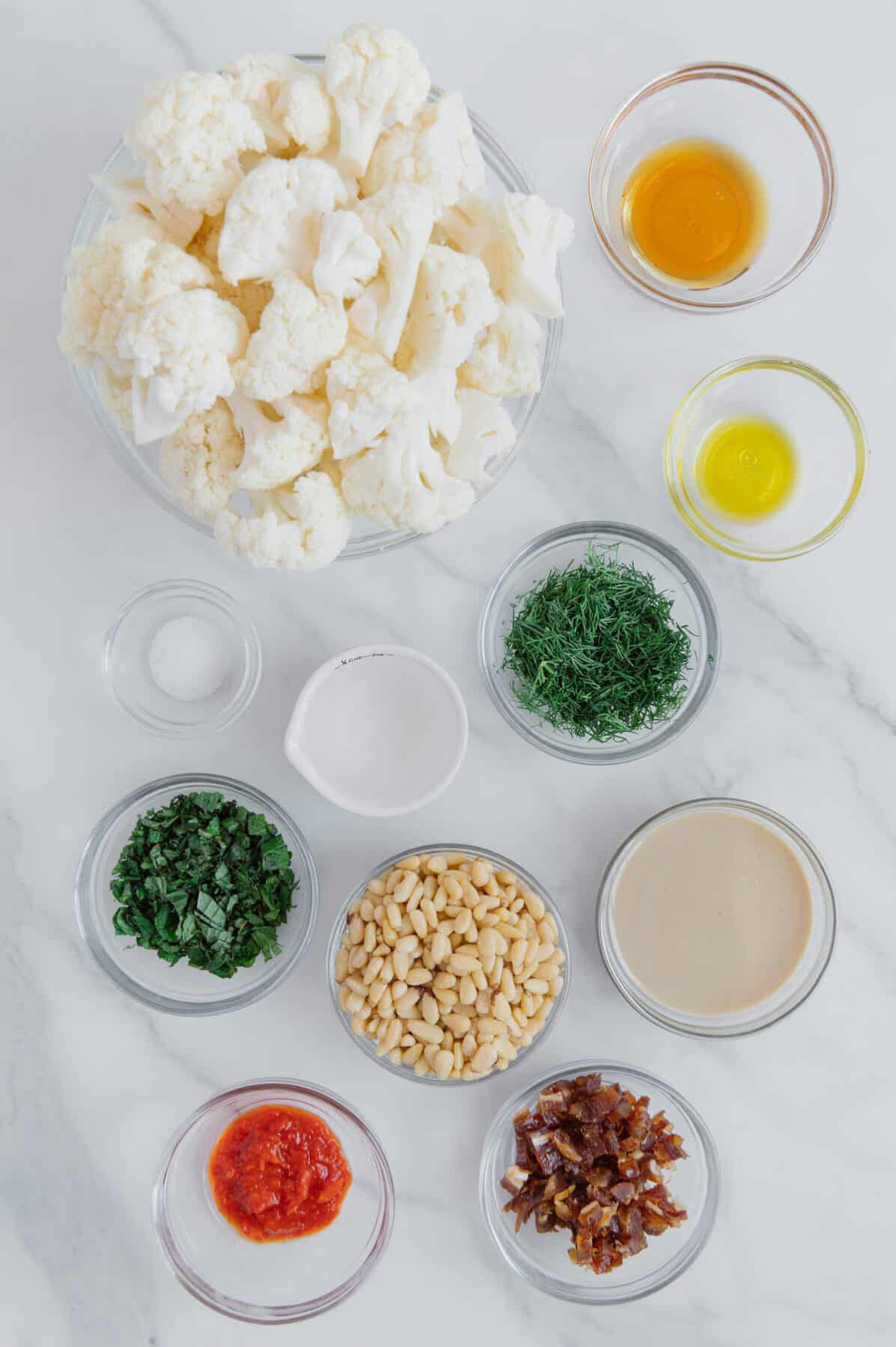 Roasted cauliflower with harissa tahini sauce ingredients with a marble white background.