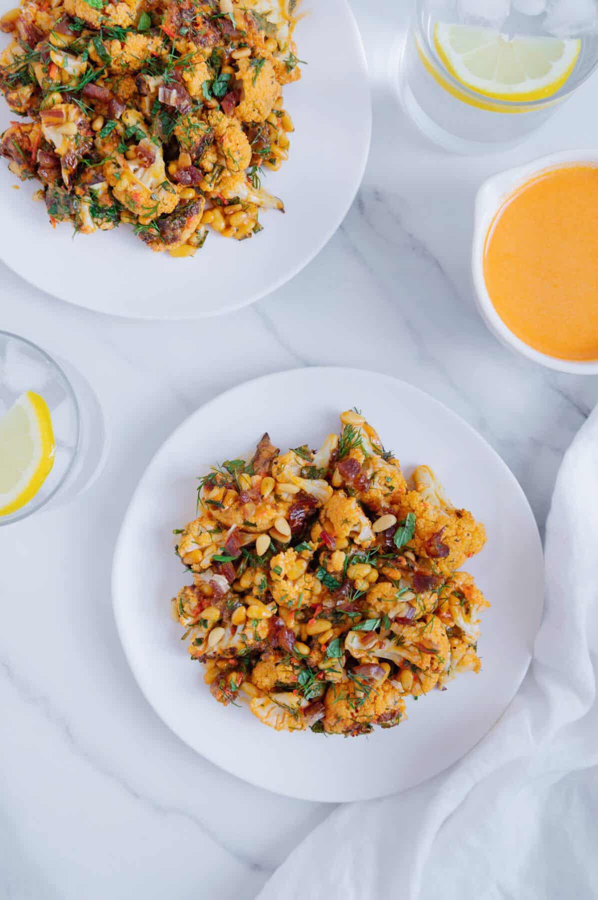 Roasted cauliflower with harissa tahini on a white plate with a marble white background.
