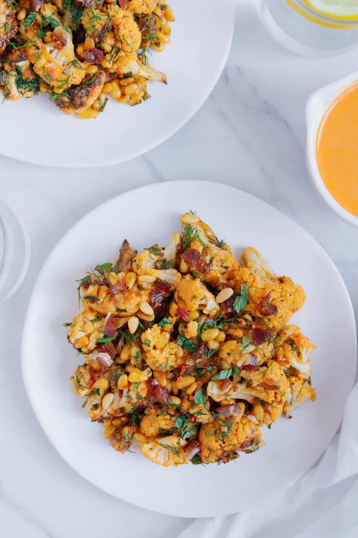Harissa tahini cauliflower served on a white plate with a marble white background.