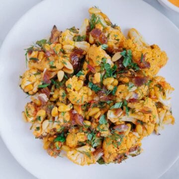 Roasted cauliflower with harissa tahini on a white plate with a marble white background.