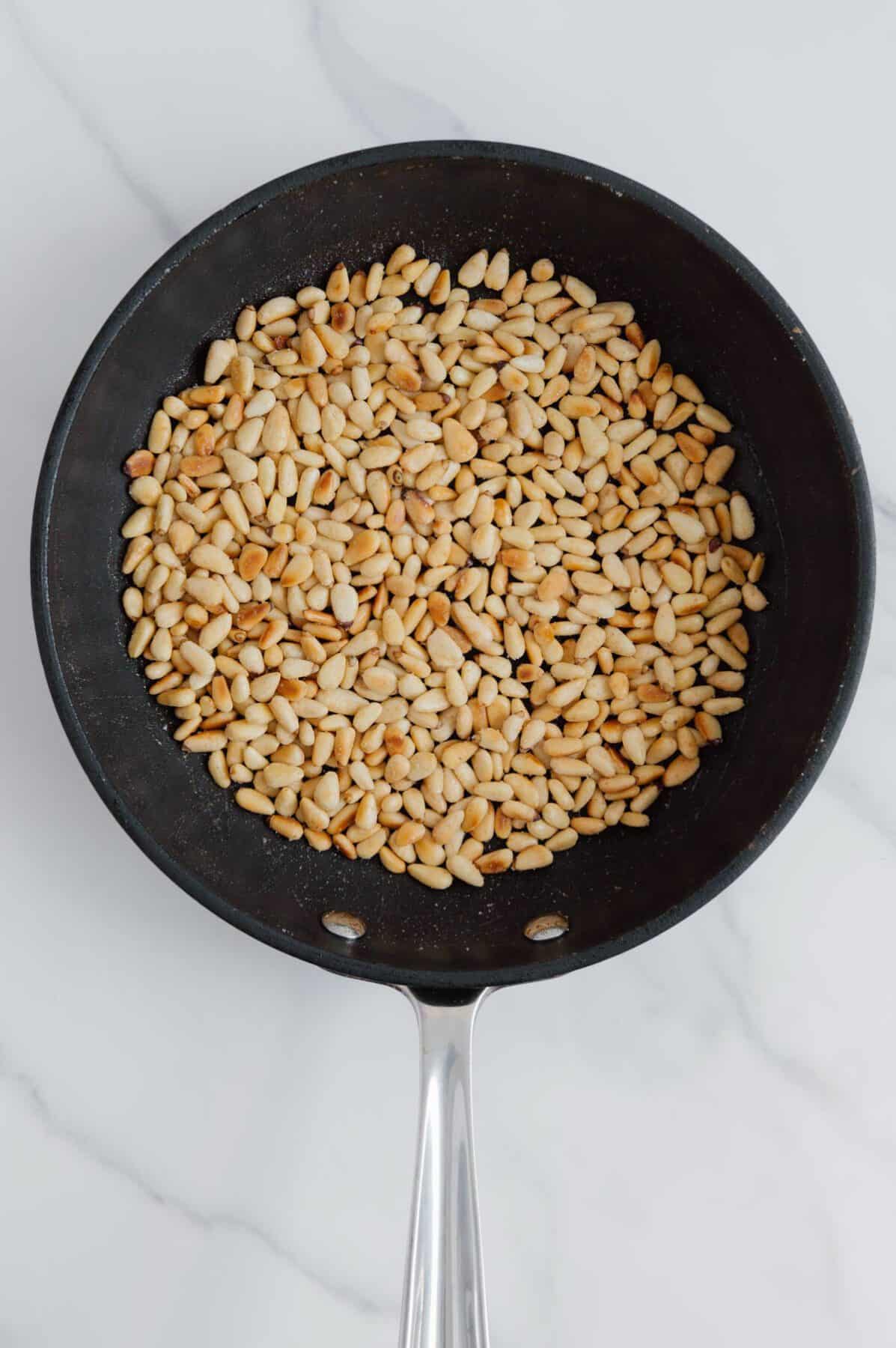 Toasted pine nuts in a skillet with a white marble background.
