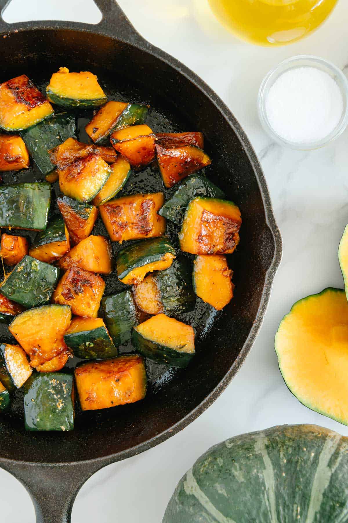 Roasted Kabocha squash in a cast iron skillet next to ingredients with a white marble background.