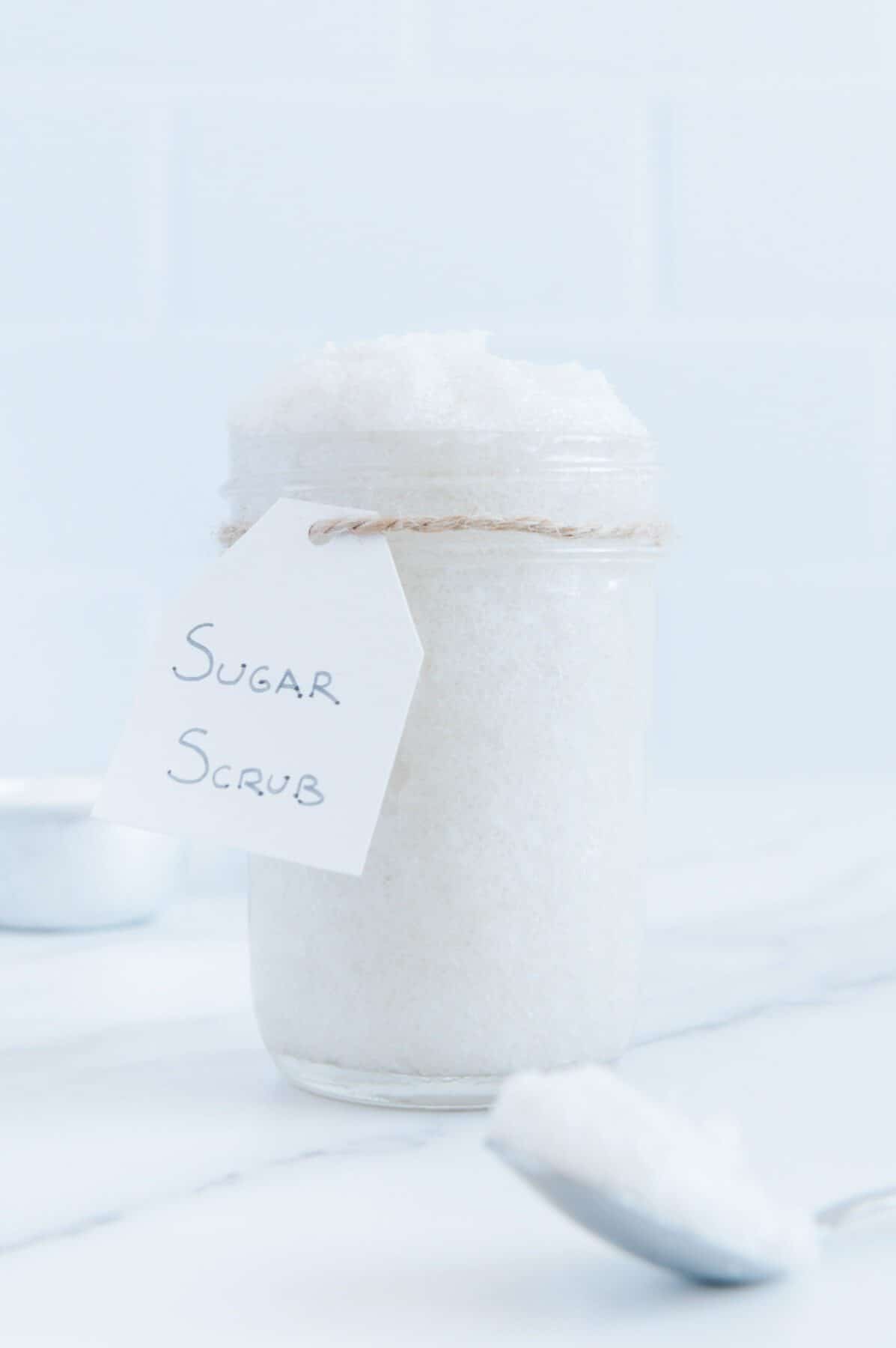 Homemade sugar scrub in a glass jar on a white counter with a white background.