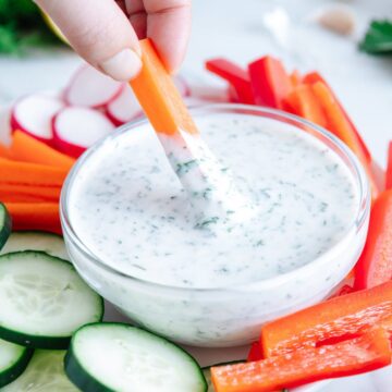 A hand dipping a raw carrot stick into vegan ranch dressing.