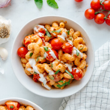 Burst cherry tomato pasta garnished with cashew cream and fresh basil in a white bowl with a white background.