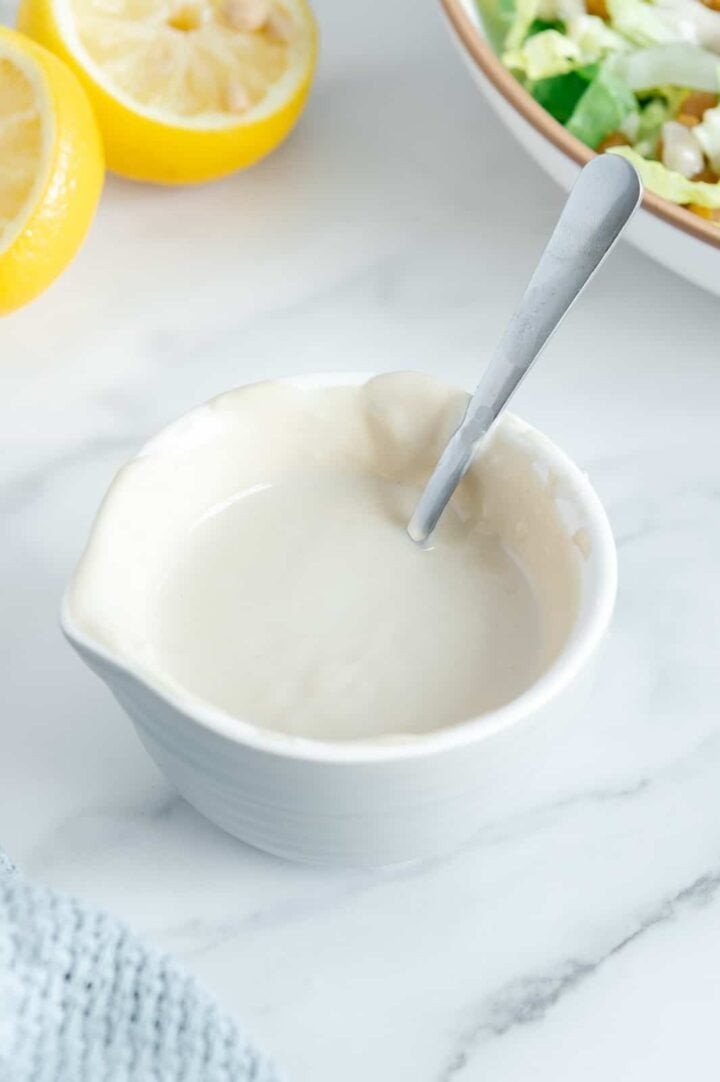 Homemade tahini salad dressing in a white bowl with a spoon dipped inside with a white background.