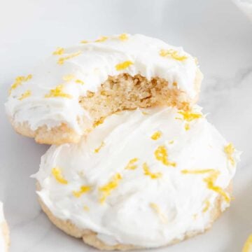 A partially eaten vegan lemon cookie on top of a whole vegan lemon cookie.
