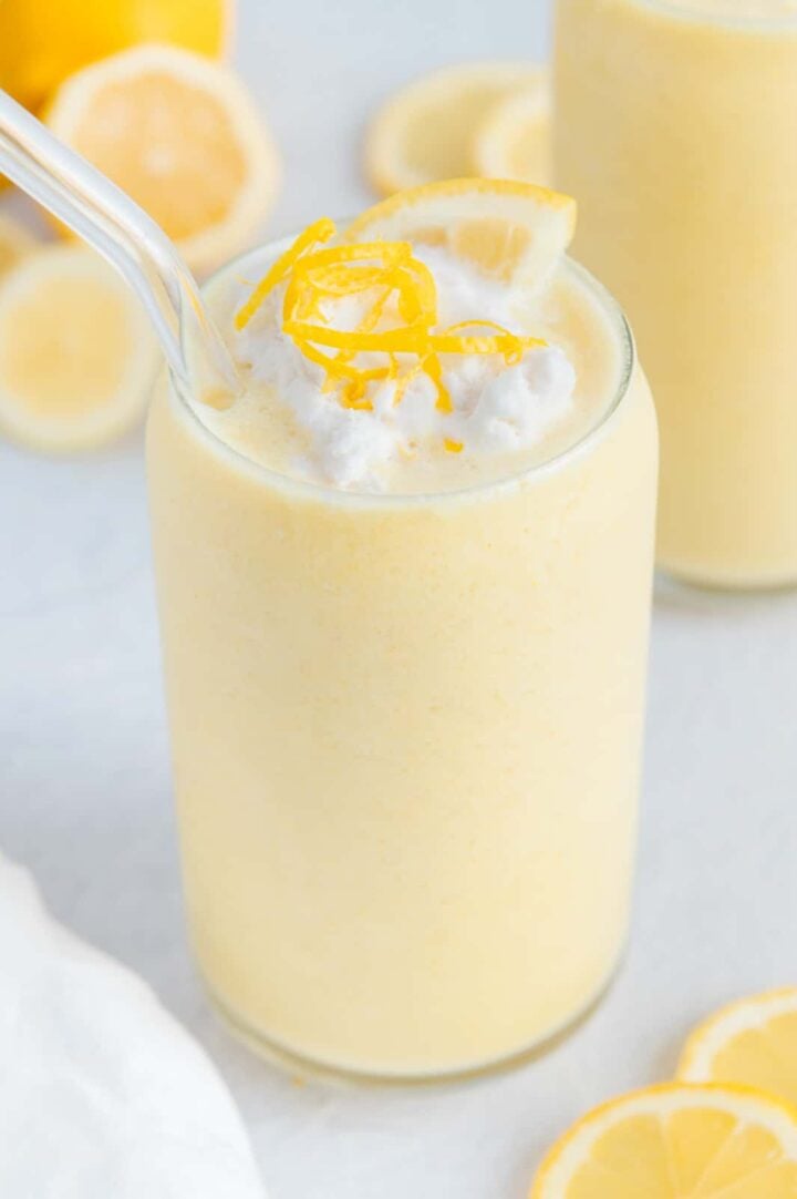 Vegan lemon smoothie garnished with coconut whipped cream and lemon zest served with a glass straw.