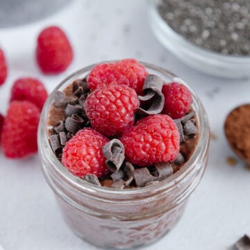 High protein chocolate chia pudding in a glass jar topped with fresh raspberries and cacao nibs.