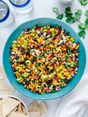 The best cowboy caviar in a large blue bowl alongside tortilla chips and fresh cilantro with a white background.