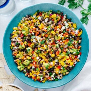 The best cowboy caviar in a large blue bowl alongside tortilla chips and fresh cilantro with a white background.