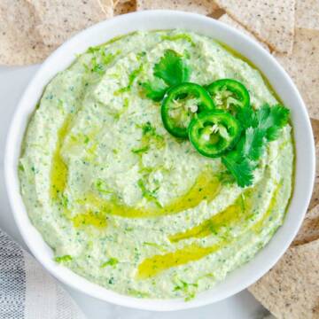 Cilantro jalapeno hummus in a white bowl served with tortilla chips.