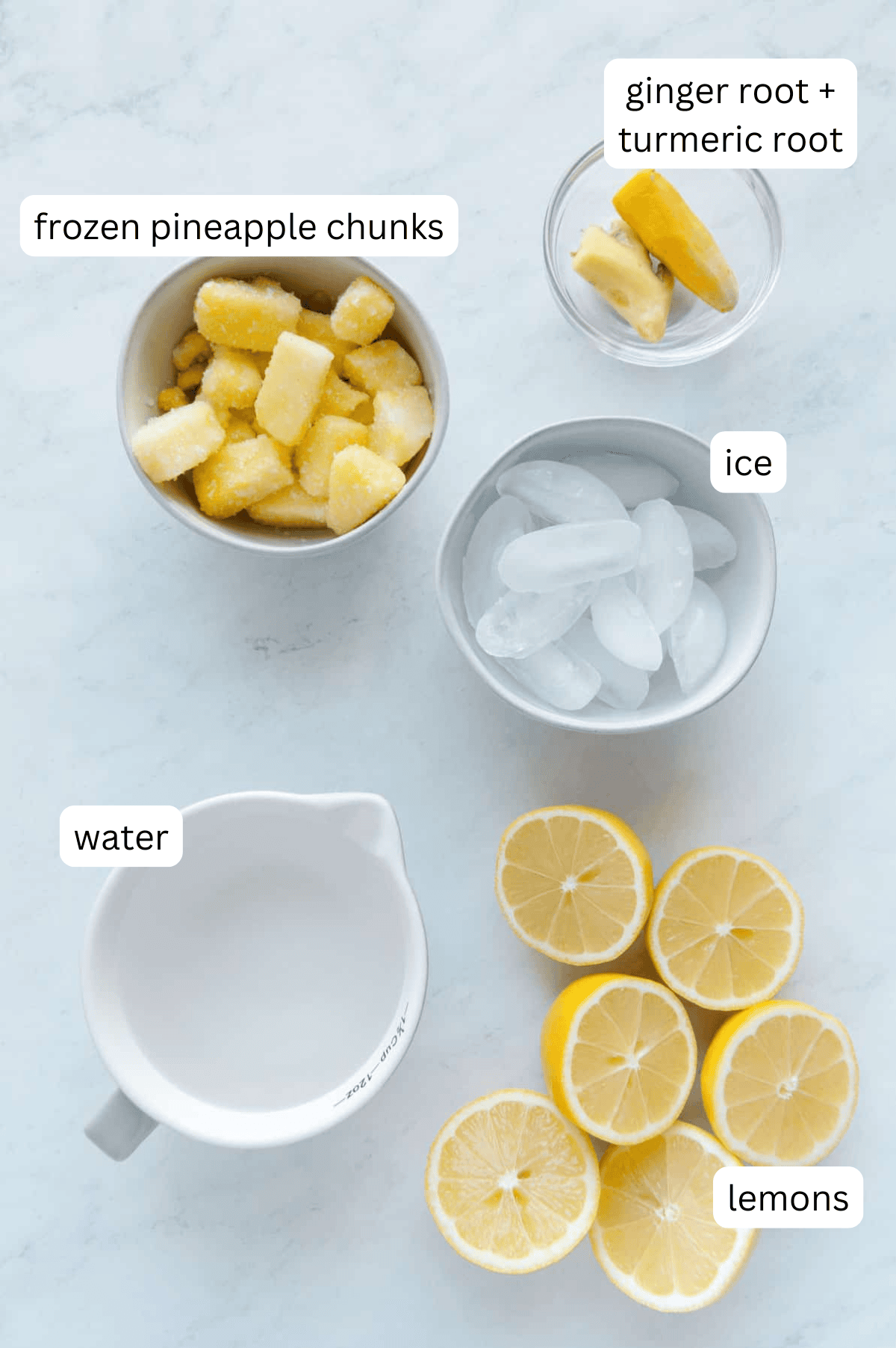 Ingredients for pineapple lemonade with ginger and turmeric with a white marble background.