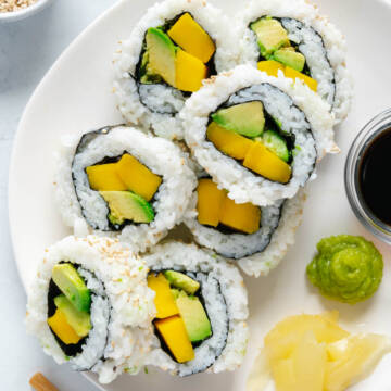 Homemade vegan sushi on a white plate served with soy sauce, wasabi and ginger.