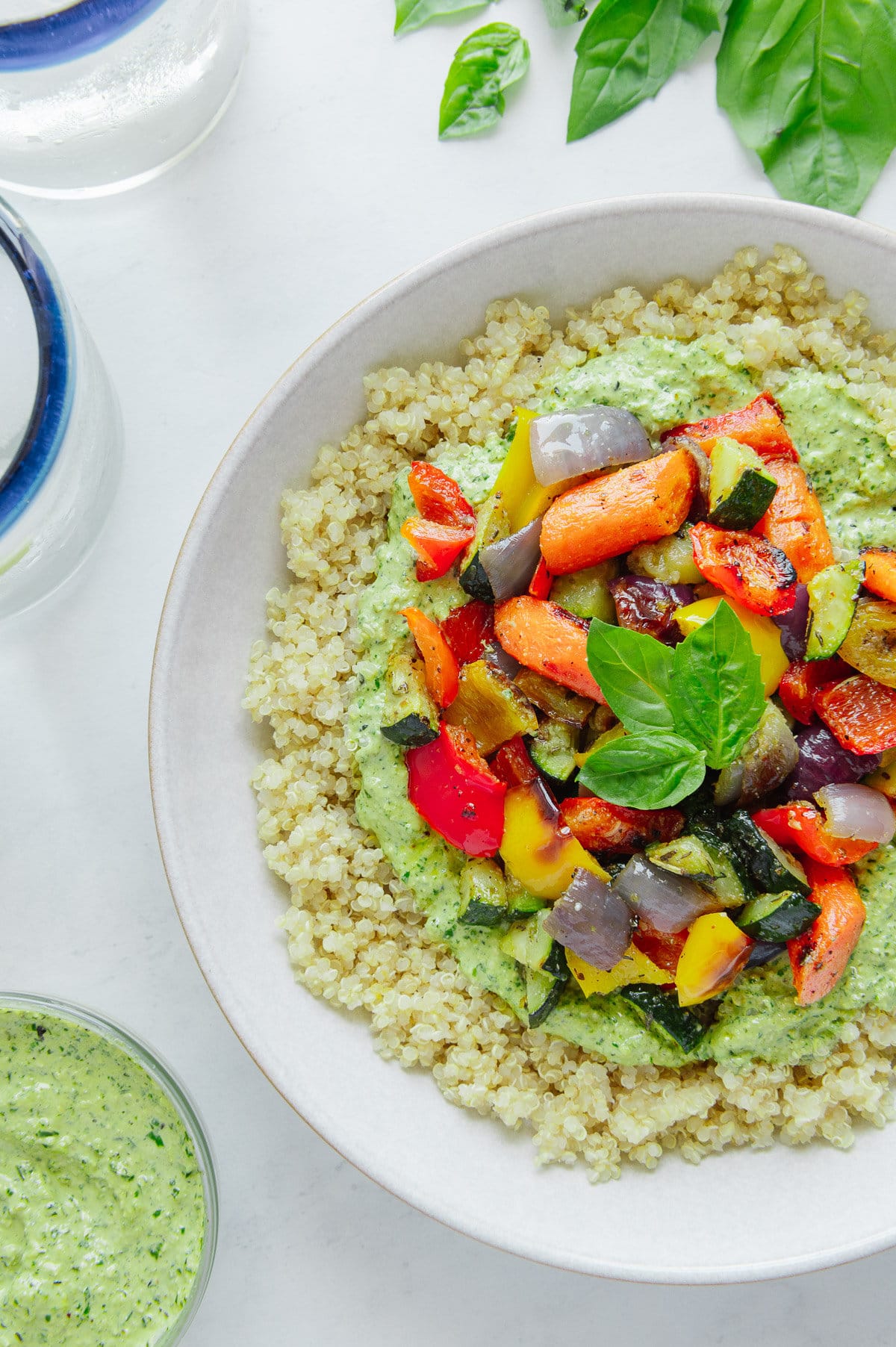 Vegan roasted vegetable quinoa bowl next to a bowl of hemp seed pesto with a white background.