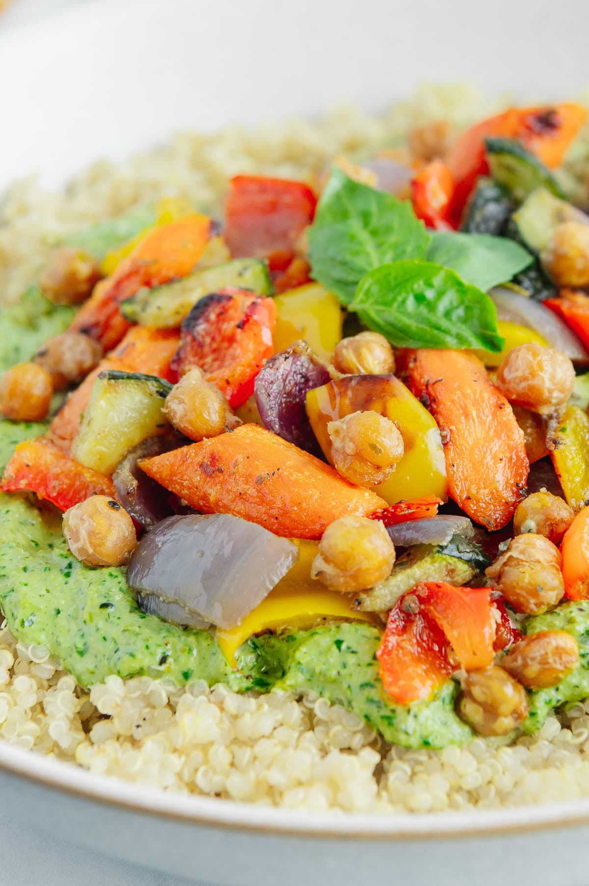 Close up of roasted vegetables including carrots, chickpeas, onions and red peppers on top of quinoa and pesto.