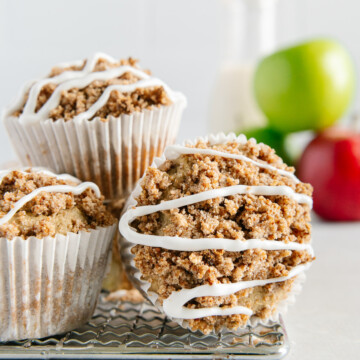 Vegan apple-cinnamin muffins next to fresh apples with a white background.