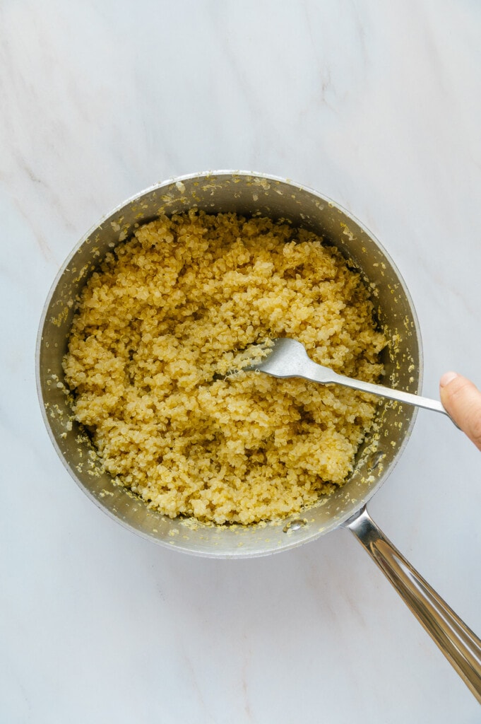 Cooked quinoa in a small saucepan with a white marble background.