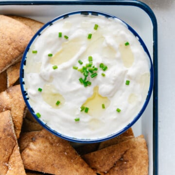 Roasted garlic dip in a bowl on a platter with pita wedges.