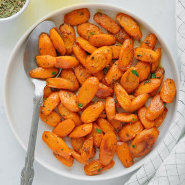 Oven-roasted carrots and a silver spoon on a white plate.