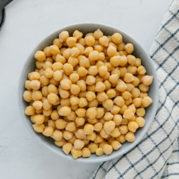 Chickpeas in a gray bowl next to a checkered towel.