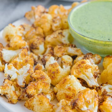 Air fryer cauliflower served with a green tahini sauce on a white plate.