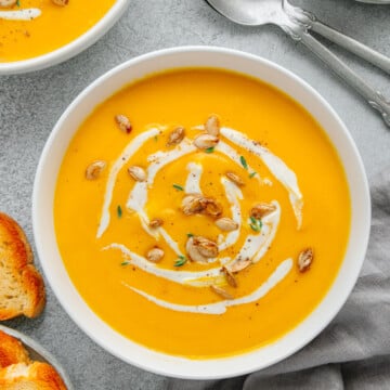 Butternut squash soup topped with roasted seeds, fresh herbs and cashew cream next to toasted crusty bread.
