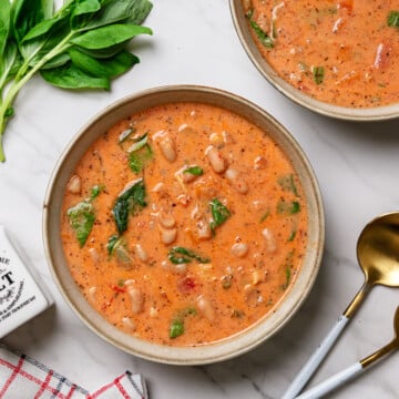 Tuscan white bean and kale soup in a bowl with a marble white background.
