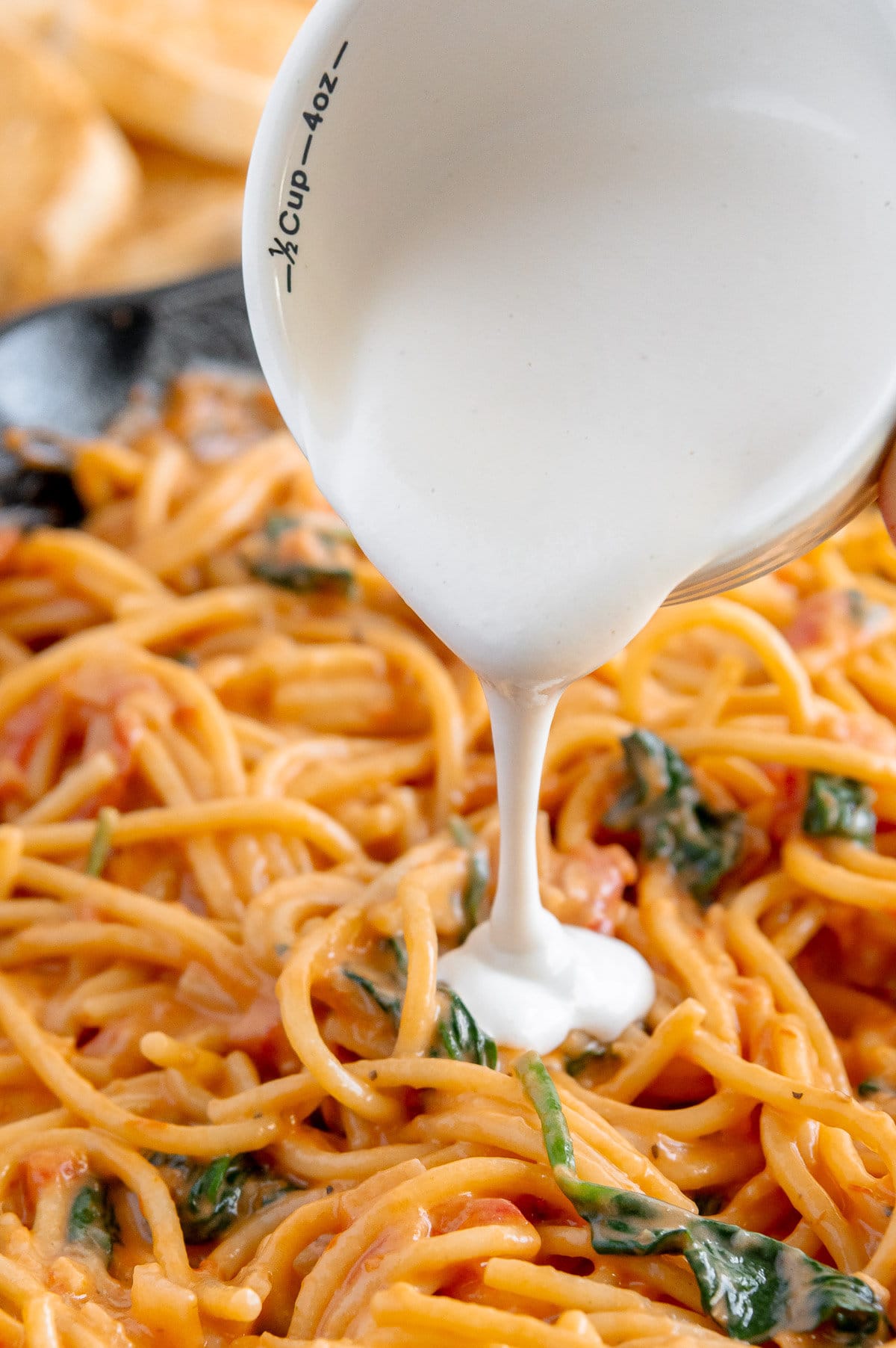 Vegan heavy cream being poured from a white bowl onto orange pasta with fresh basil.