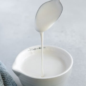 Vegan heavy cream dripping from a spoon into a white cup with a white background.