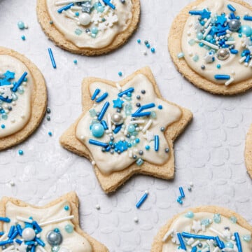 Hanukkah sugar cookies topped with white icing and blue sprinkles on a sheet of white parchment paper.