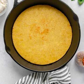 Chickpea flour pizza crust in a cast iron skillet next to tomato sauce and fresh basil with a white background.