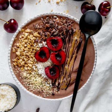 Chocolate acai protein bowl topped with cacao nibs, cherries and seeds.